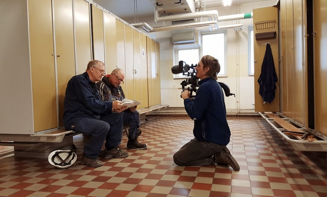 Himlens mörkrum Två män på en bänk i ett omklädningsrum med en kameraman framför sig